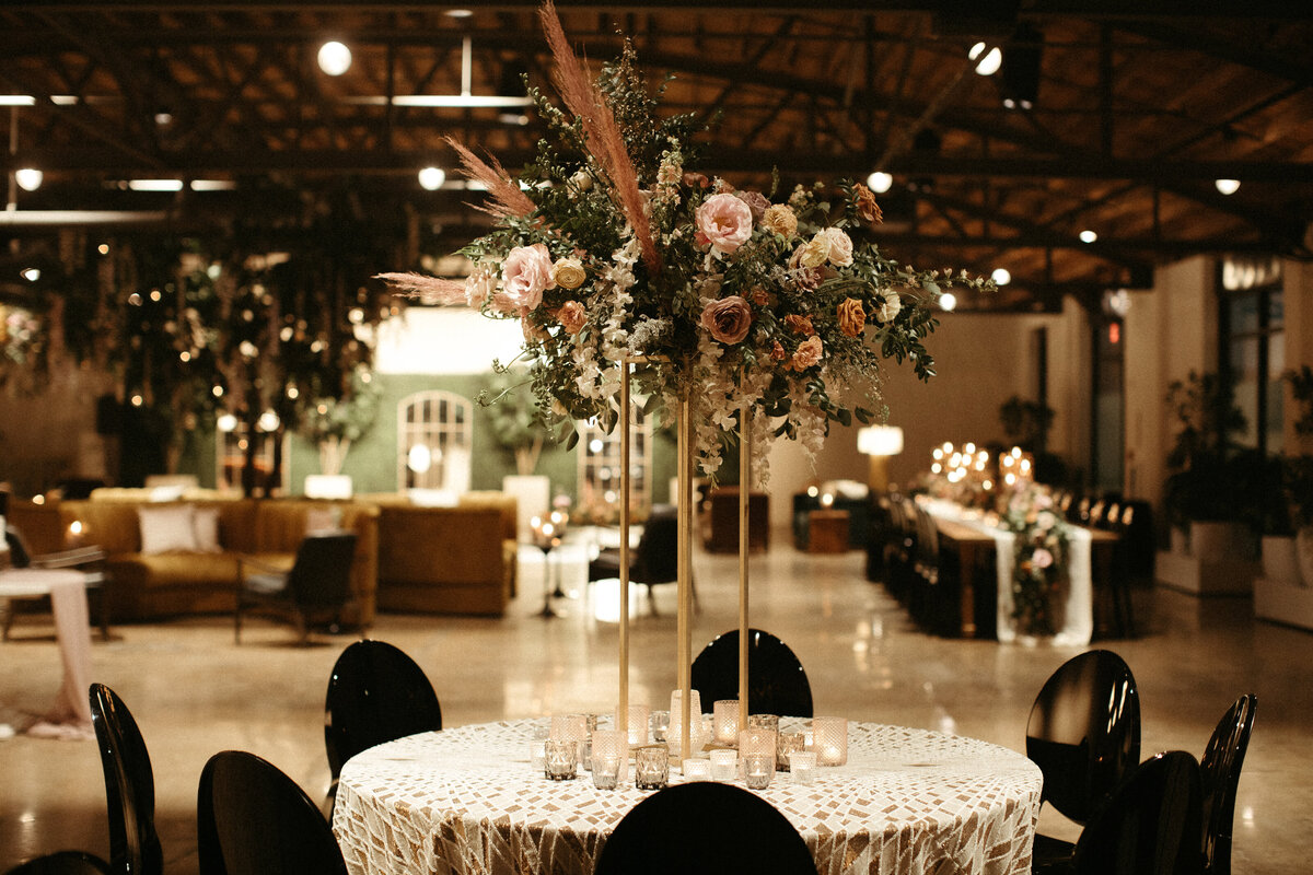 Stunning elevated centerpieces decorate this art deco wedding. Floral hues of terra cotta, mauve, burgundy, and dusty pink are brought to life with petal heavy roses, dried branches, and pink pampas grass. Designed by Rosemary and Finch in Nashville.