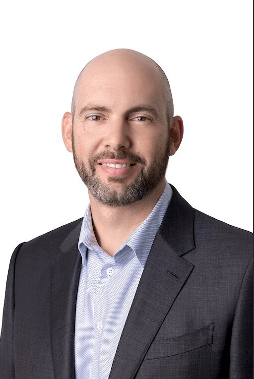 Professional Headshot of a man wearing a suit without a tie on a white background smiling at the camera
