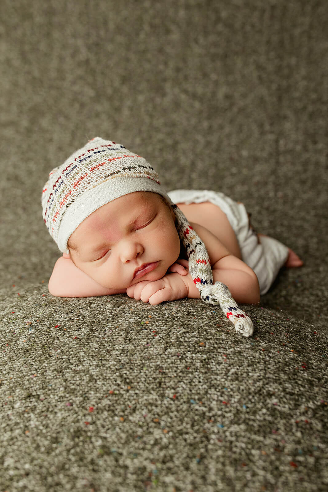 A close-up of a sleeping baby wrapped in a dark blue swaddle, with their hands gently clasped under their chin. The baby is wearing a matching knit bonnet. They are resting on a plaid blanket with soft colors in a vintage metal basket, showcasing a calm and serene atmosphere.