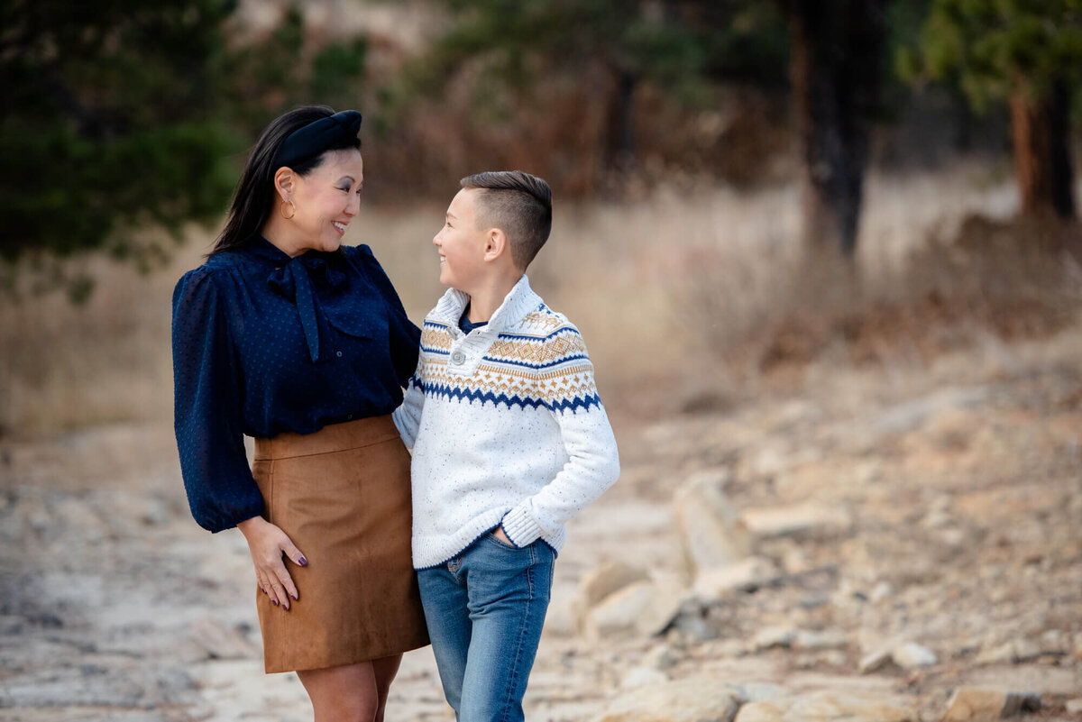 A mother stands with her son with arms around each other and smile at each other