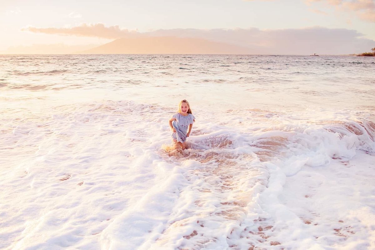 Love + Water Photography image of girl laughing on the beach as waves wash over her