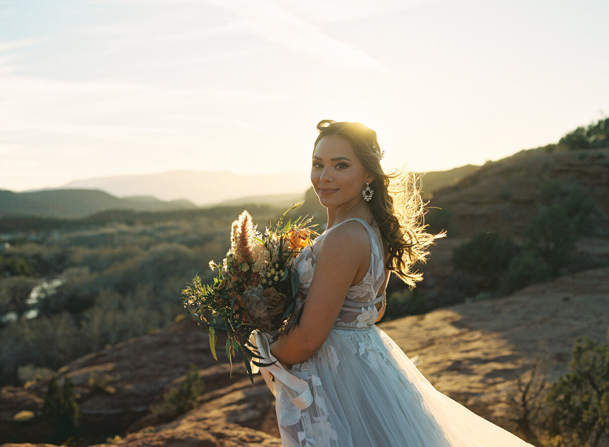 a bride in her wedding dress holding flowers in the sun
