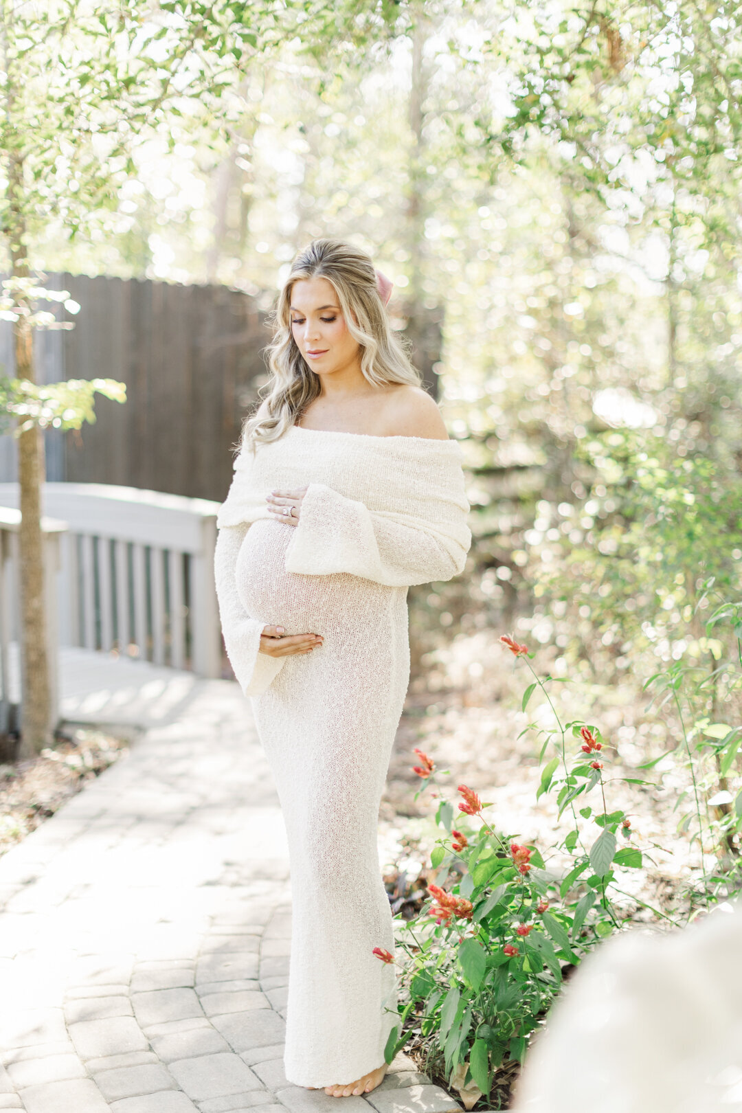 mom holds belly and glances down in garden for maternity photo session