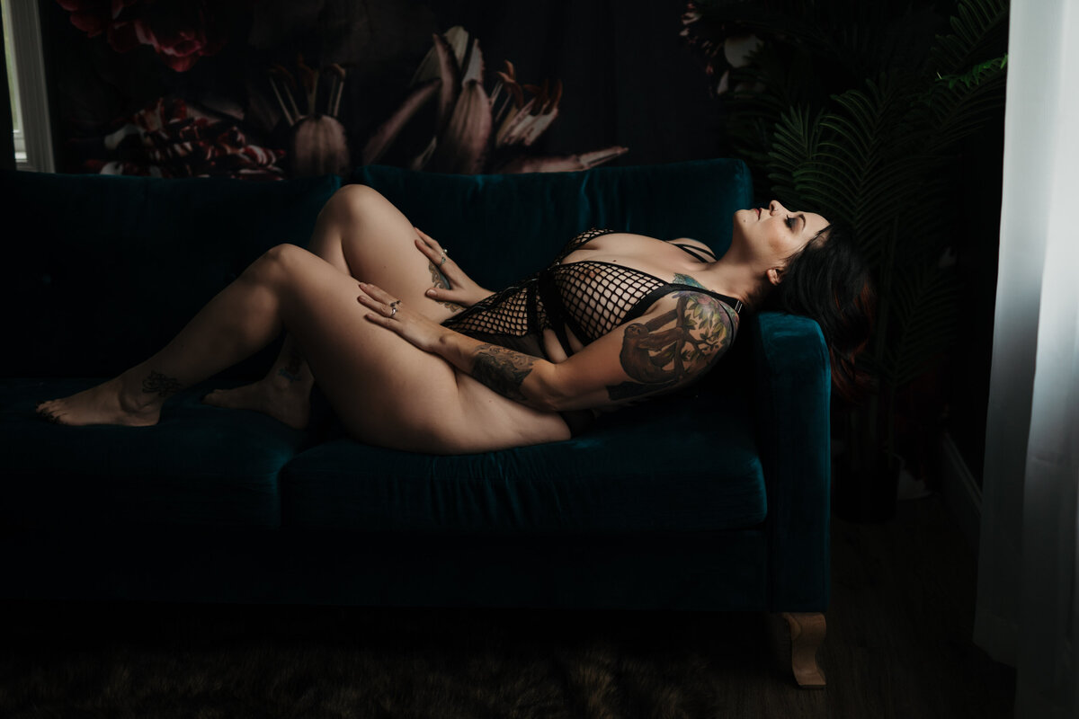 A woman in black mesh lingerie lays in a pool of sunlight on a blue couch