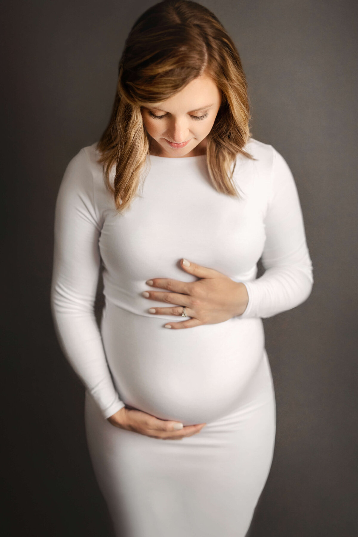 pregnant mother wearing a white maternity dress holding her baby bump in an in-studio maternity session