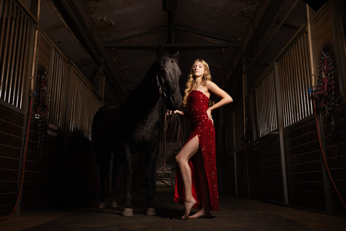 A senior girl in a red sequin dress poses with her horse in a barn, captured by a Dallas senior photographer.