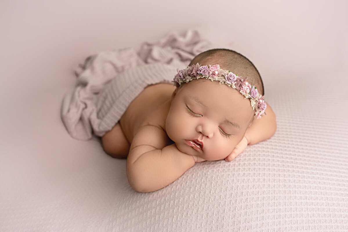 newborn baby girl poses on purple backdrop with chin on hands, hamilton, ON