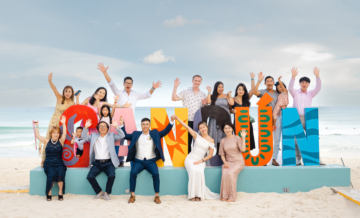 A happy wedding party by a Cancun sign with a destination wedding photographer