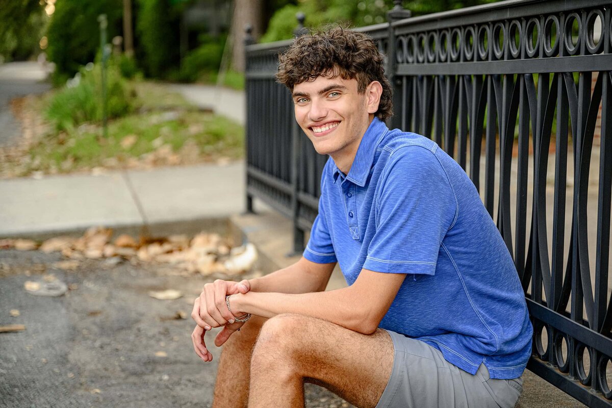 blue eyed senior boy from cuthbertson high school sits in a downtown area during his charlotte graduation photos 