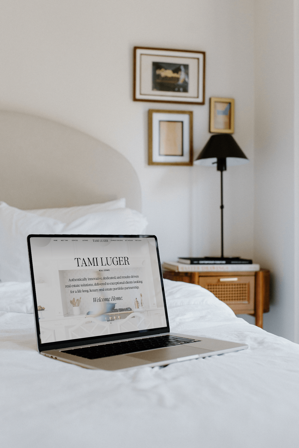 A laptop displaying a Showit website rests on a bed in a minimally decorated bedroom with framed pictures, a lamp, and a nightstand, perfectly capturing the brand identity meticulously crafted by Sweet Pea Ink Creative.