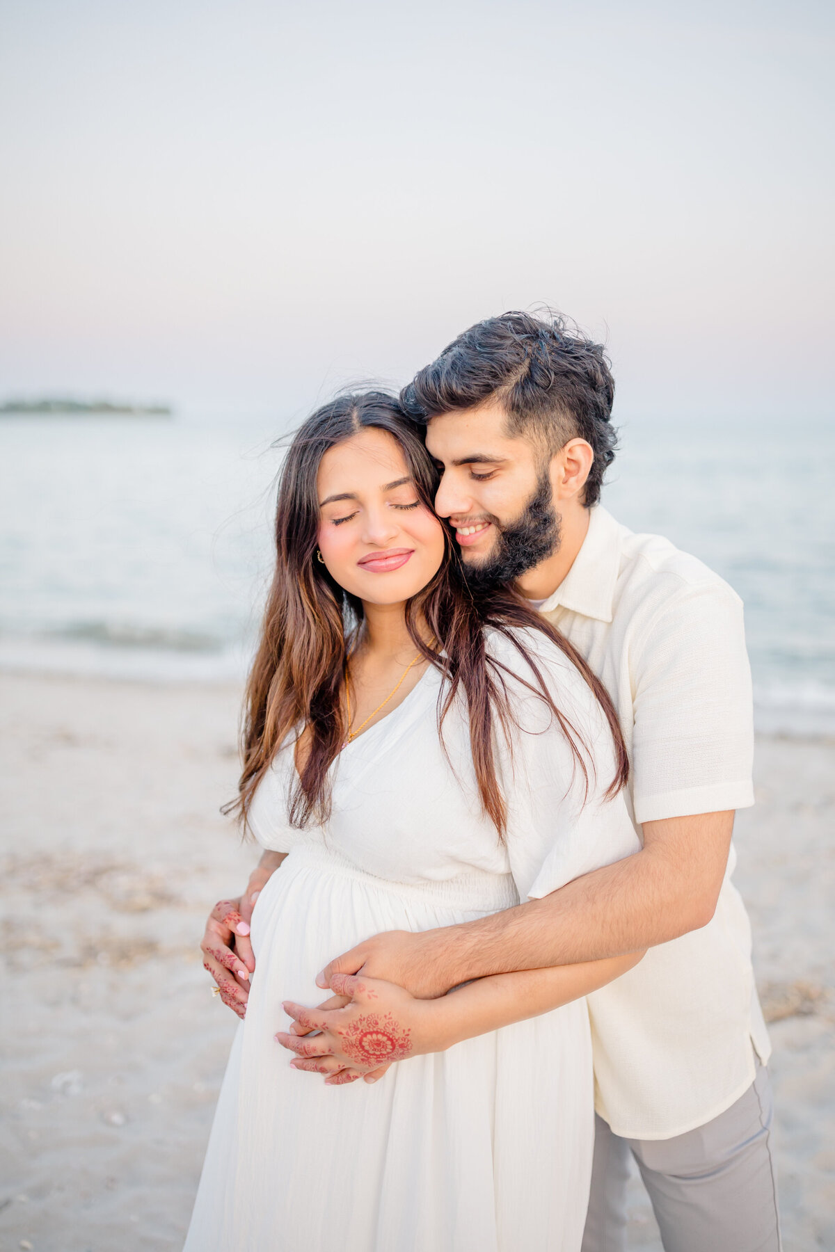 a husband hugs his pregnant wife around her back and has his hands on her pregnant belly, by Oak and Lore Studios in Connecticut