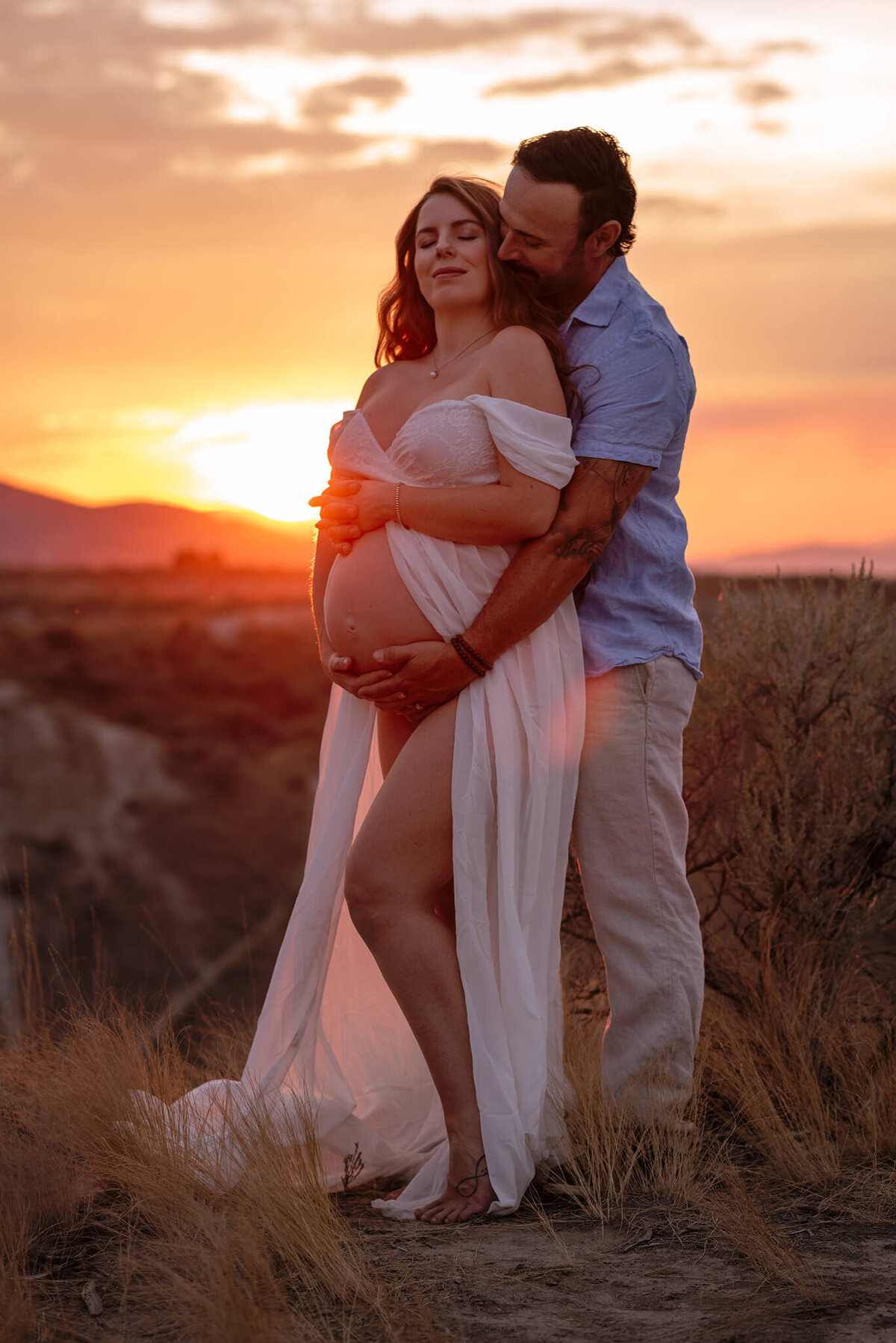 A dramatic portrait of a maternity couple. A husband embraces his wife from behind, caressing her belly and snuggling into her neck. Taken by Brittany Danielle.