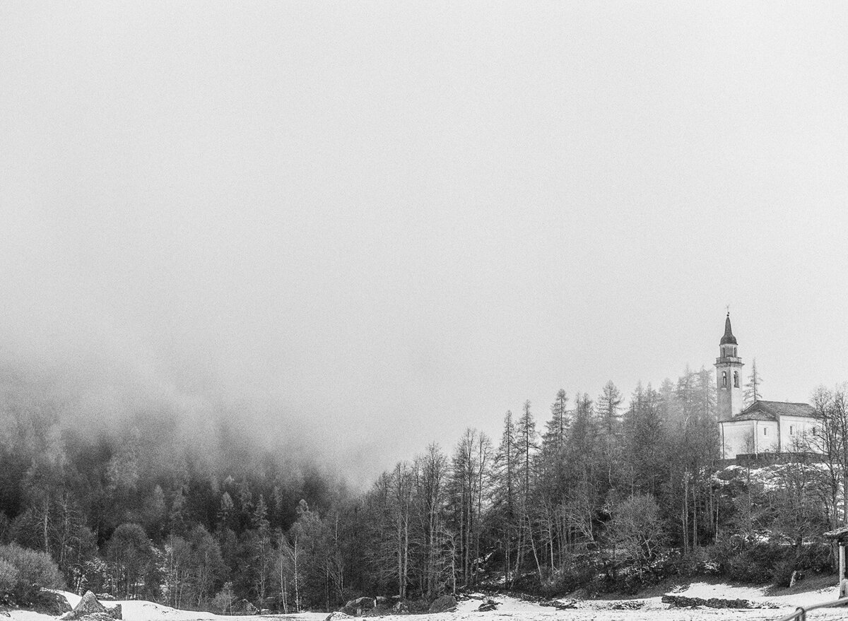 Black and white film photograph of church in the Alps in Switzerland surrounded by fog