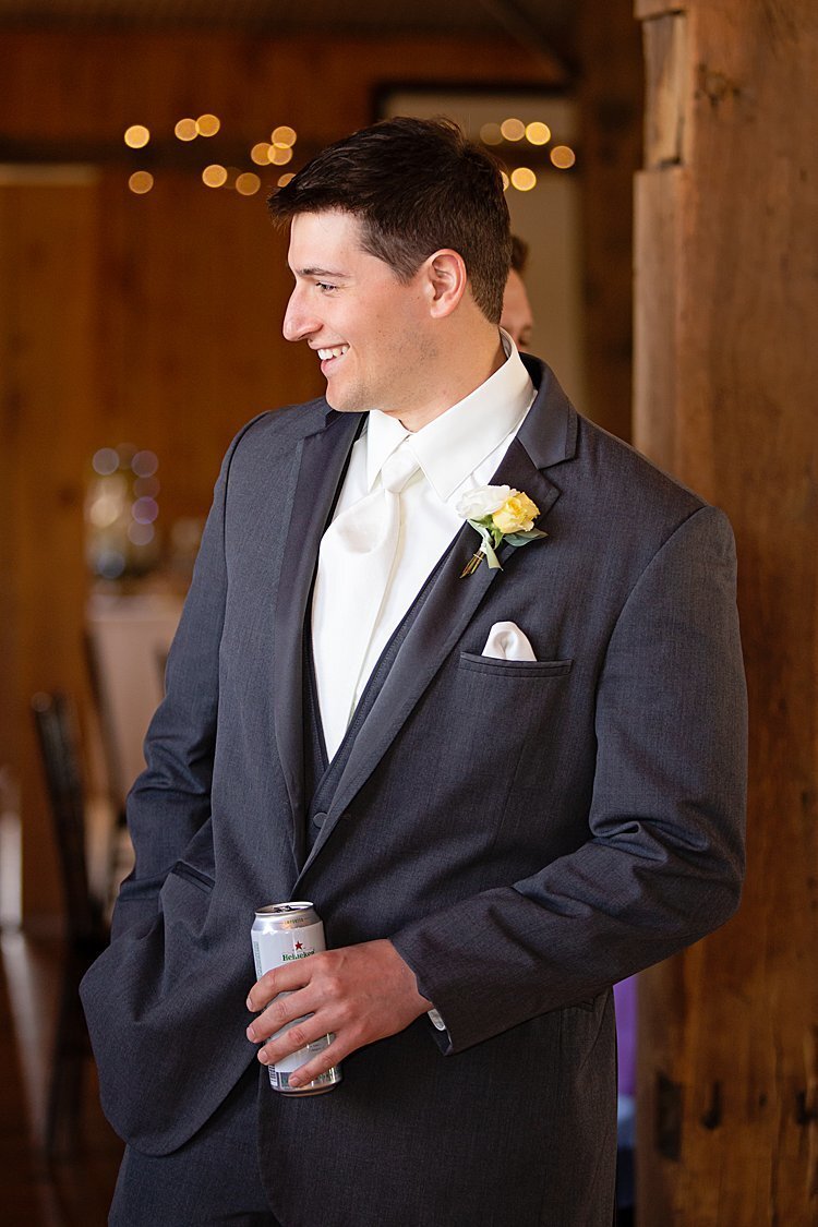 Groom leaning against pole enjoying a beverage before his wedding ceremony at White Barn in Prospect, PA