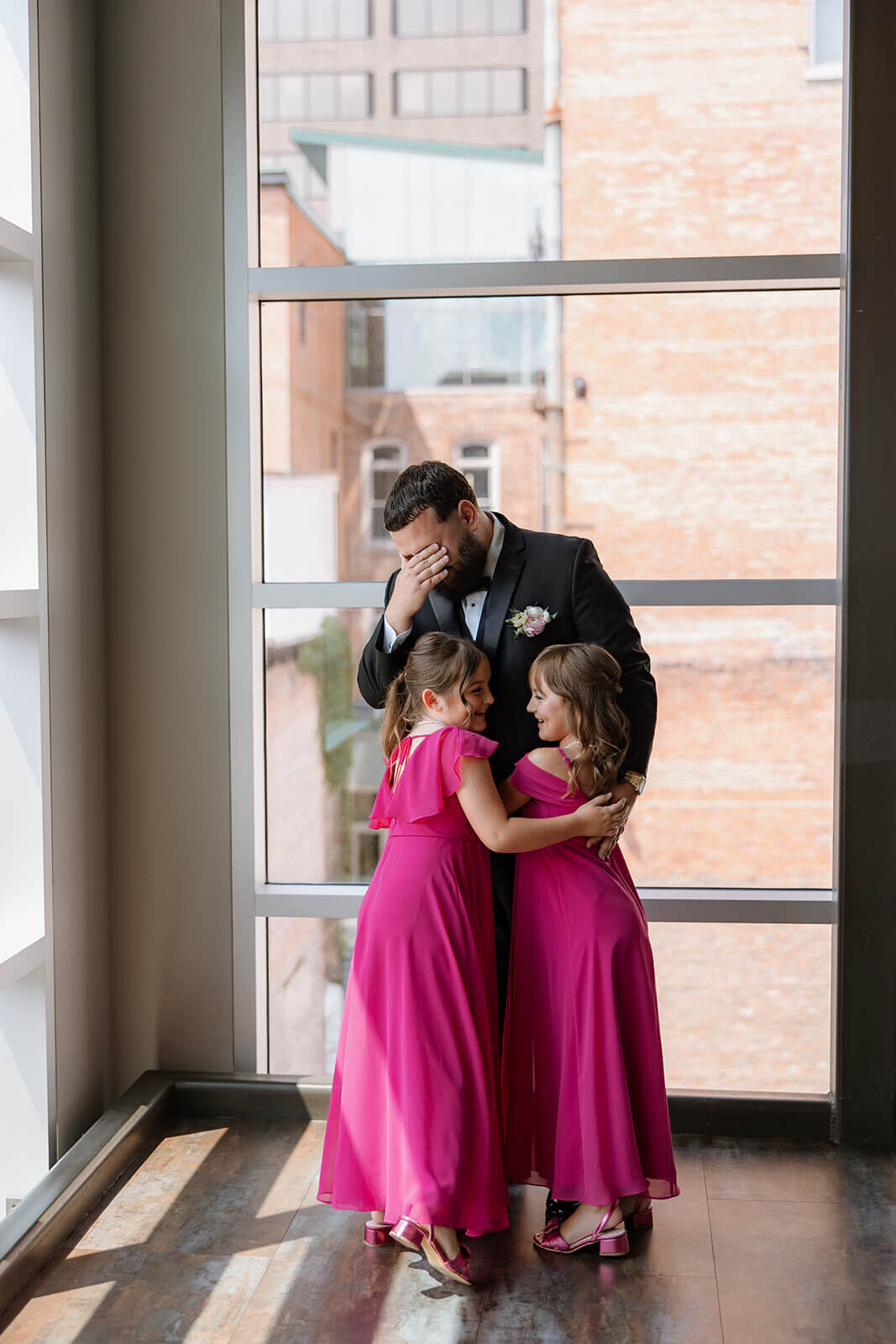 Bridemsaids in pink dresses hugging a man who looks emotional