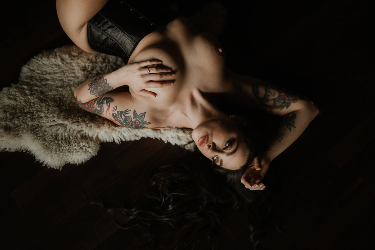 Woman wearing a black corset lays on her back on the floor in the Vancouver, BC boudoir studio.