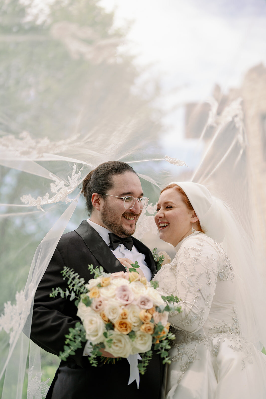 Close-up of bride and groom holding hands showing floral bouquet, rings, and gown details during their Henry Ford Estate wedding.