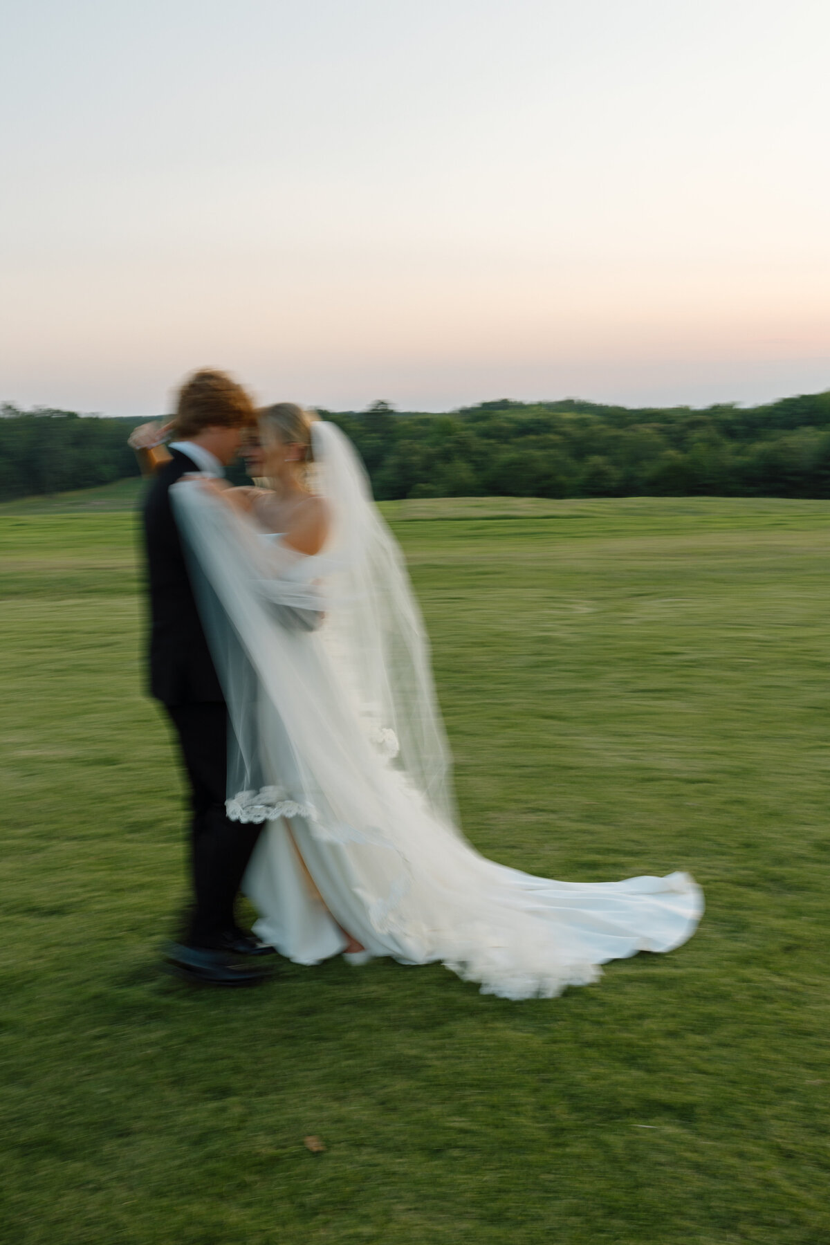 Bride and groom hug each other as bride holds her veil