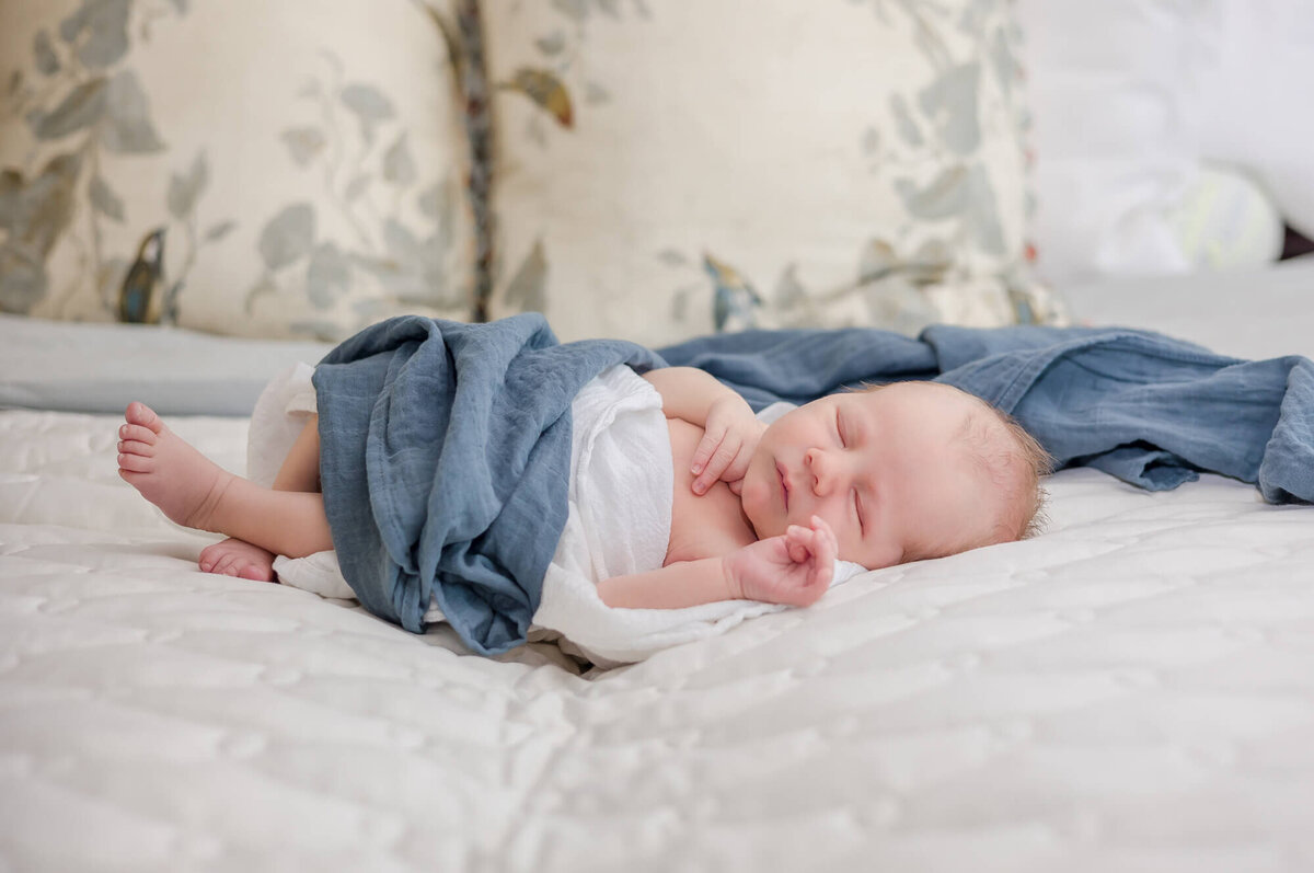 newborn baby boy wrapped in blue and white blankets sleeping on a bed