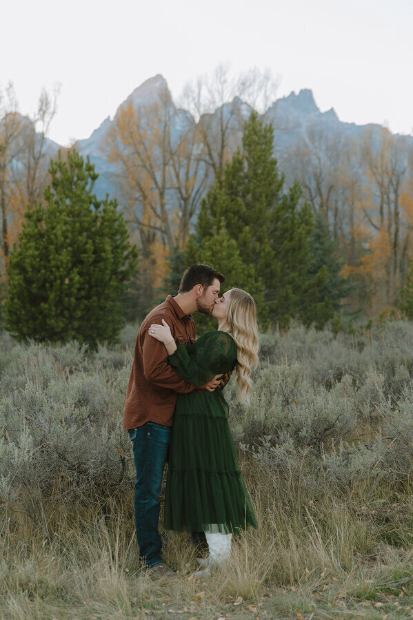 An engaged couple kisses with the view of the Grand Tetons behind them near Jackson WY.