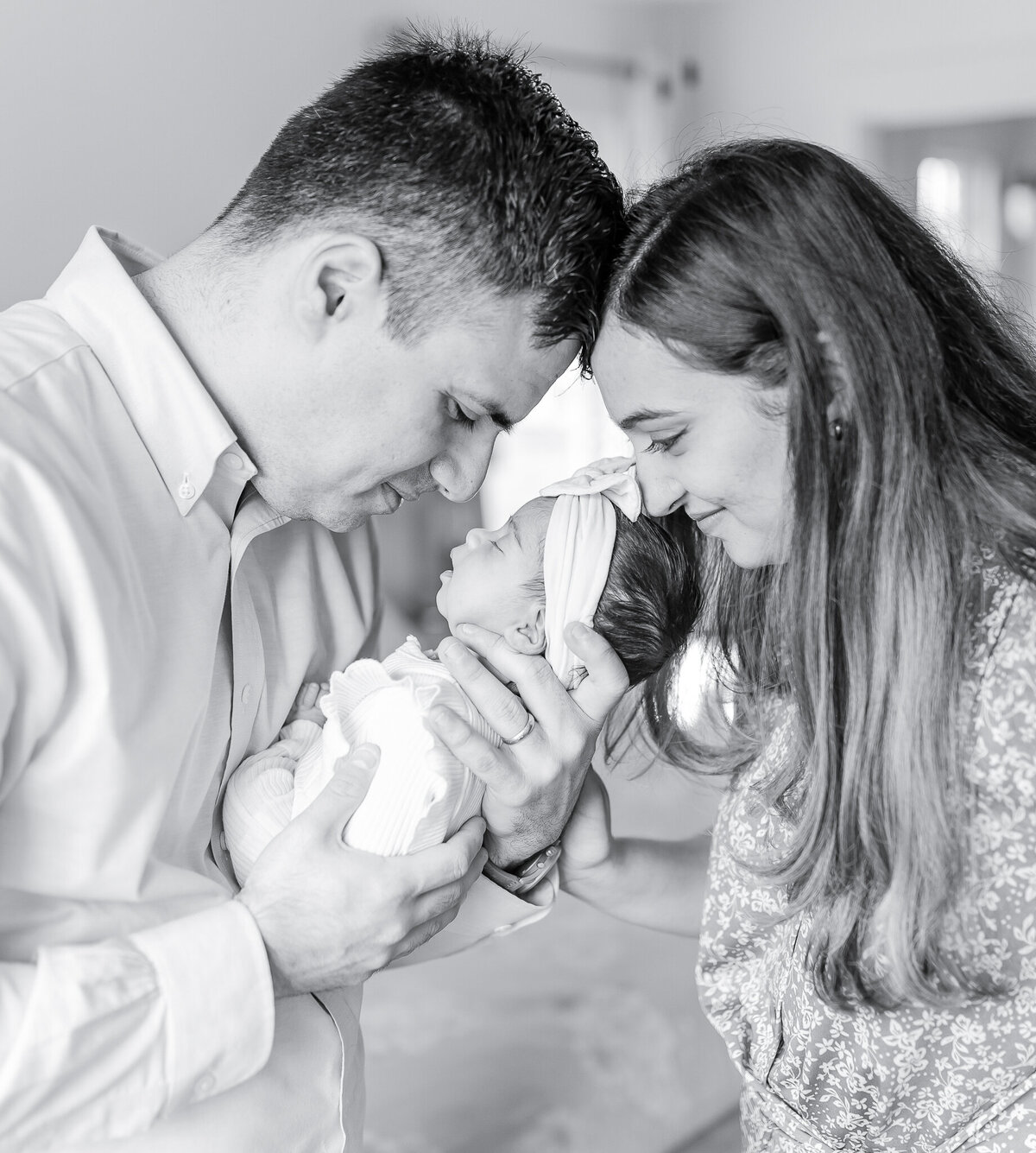 Black and white lifestyle newborn photography featuring a loving couple holding their sleeping baby girl. This intimate family moment highlights the joy of welcoming a newborn at home