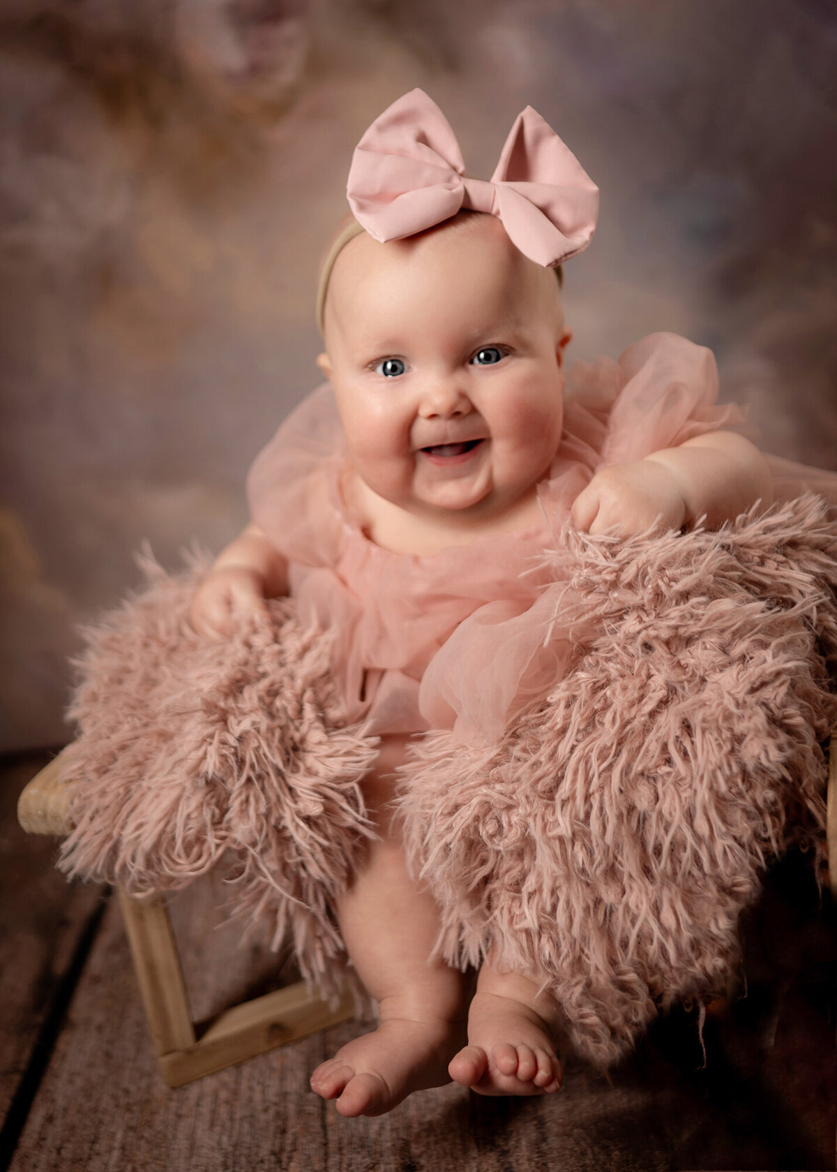 A baby girl laughs while she sits on a fluffy pink chair and wears a pink tutu