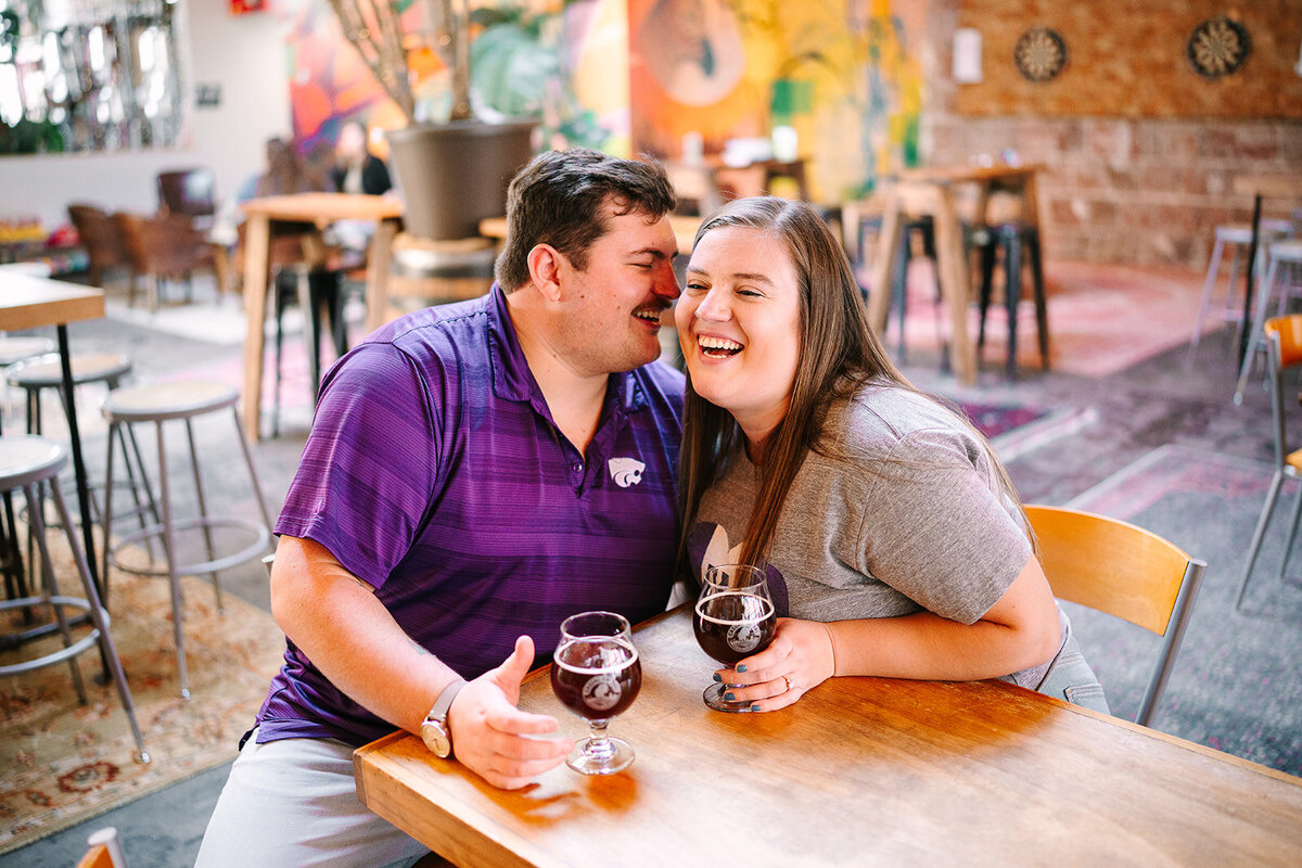 A couple sitting at a table in a brewery as one leans into the other 