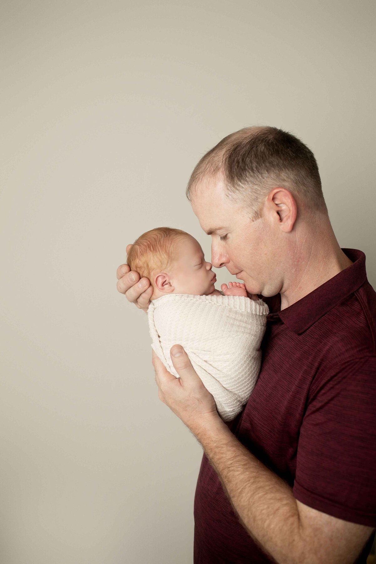 Dad lovingly holding his newborn son in his arms, looking down at him with a smile