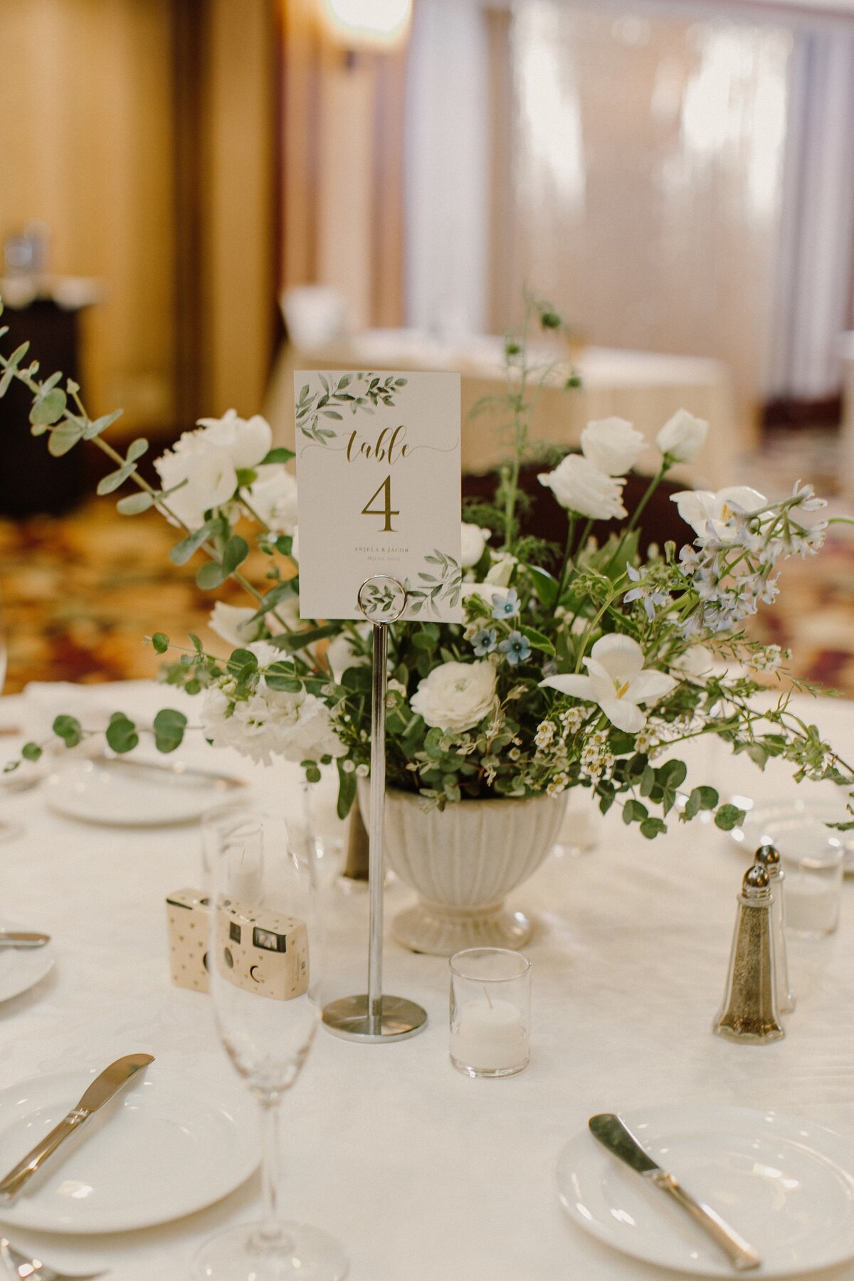 White table number and white and greenery floral centerpiece at a wedding reception.