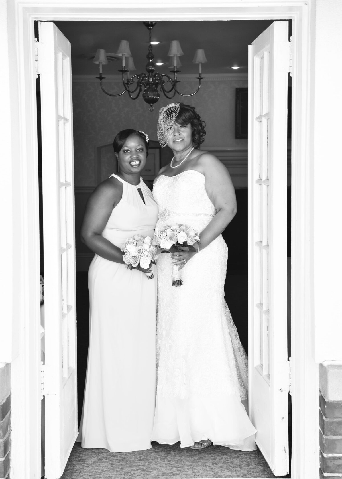 Bride and bridesmaid posing together in doorway, smiling.