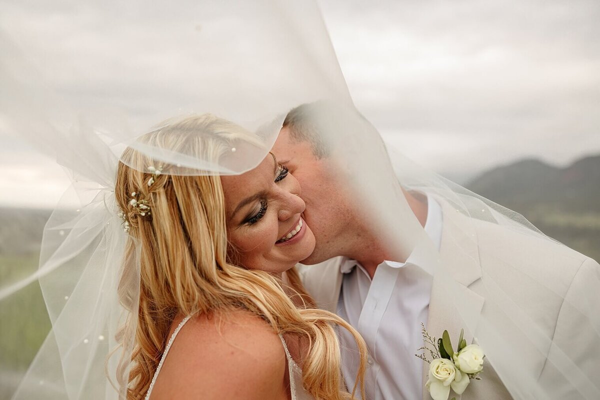 Bride and groom couple portrait with groom kissing her cheek and bride smiling. In Colorado Springs, CO