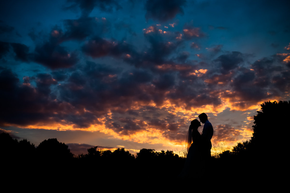 The couple stands silhouetted against a beautiful sunset after marrying at Shady Lane Farm in Maine