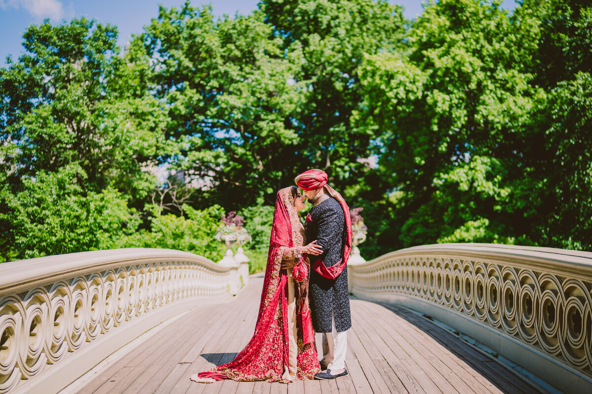 A pakistani muslim wedding couple wearing red sharing a moment during their elopement at central park on the bow bridge