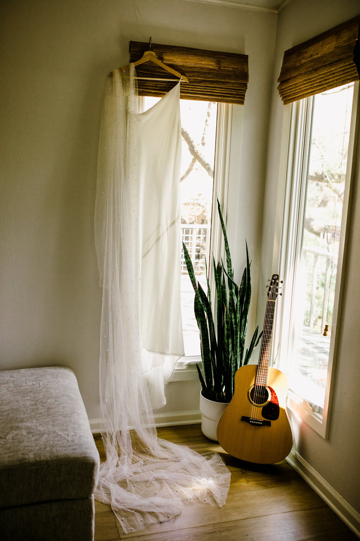 Wedding dress hanging from window next to snake plant and guitar
