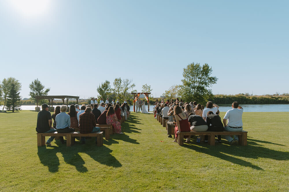 A shot looking down the aisle at an outdoor wedding ceremony in Swan Valley, Idaho. The guests are seated and the bride and groom are standing at the front.