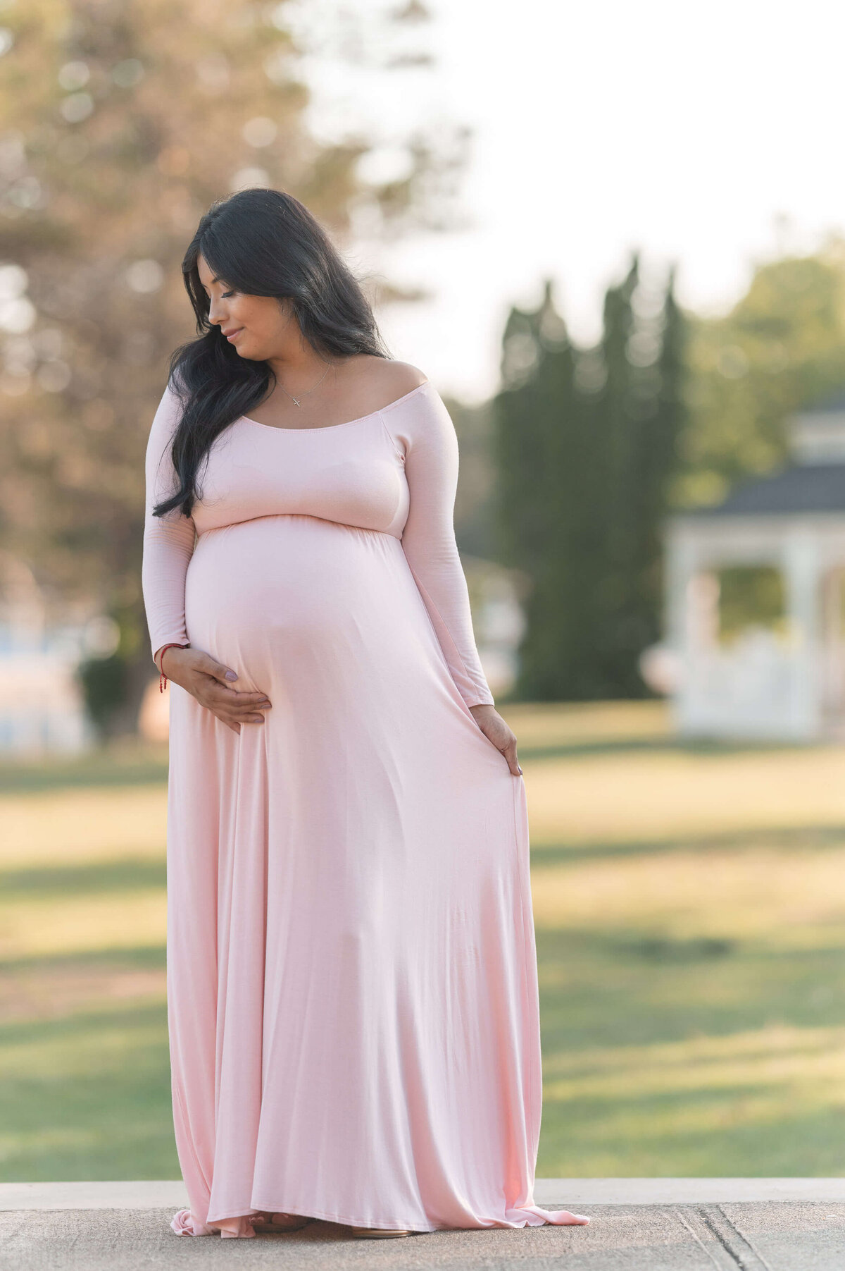 pink maternity dress on a beautiful mom standing on a plataform smealing her long dark hair