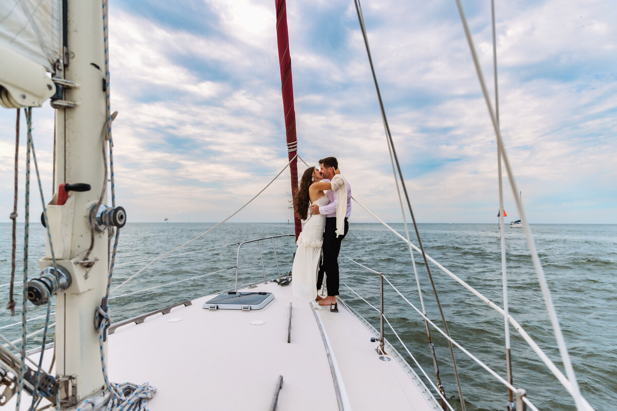 Shannon Lee, from Love Like Wild Photography, captures a couple embracing on the deck of a sailboat against a vast ocean backdrop.