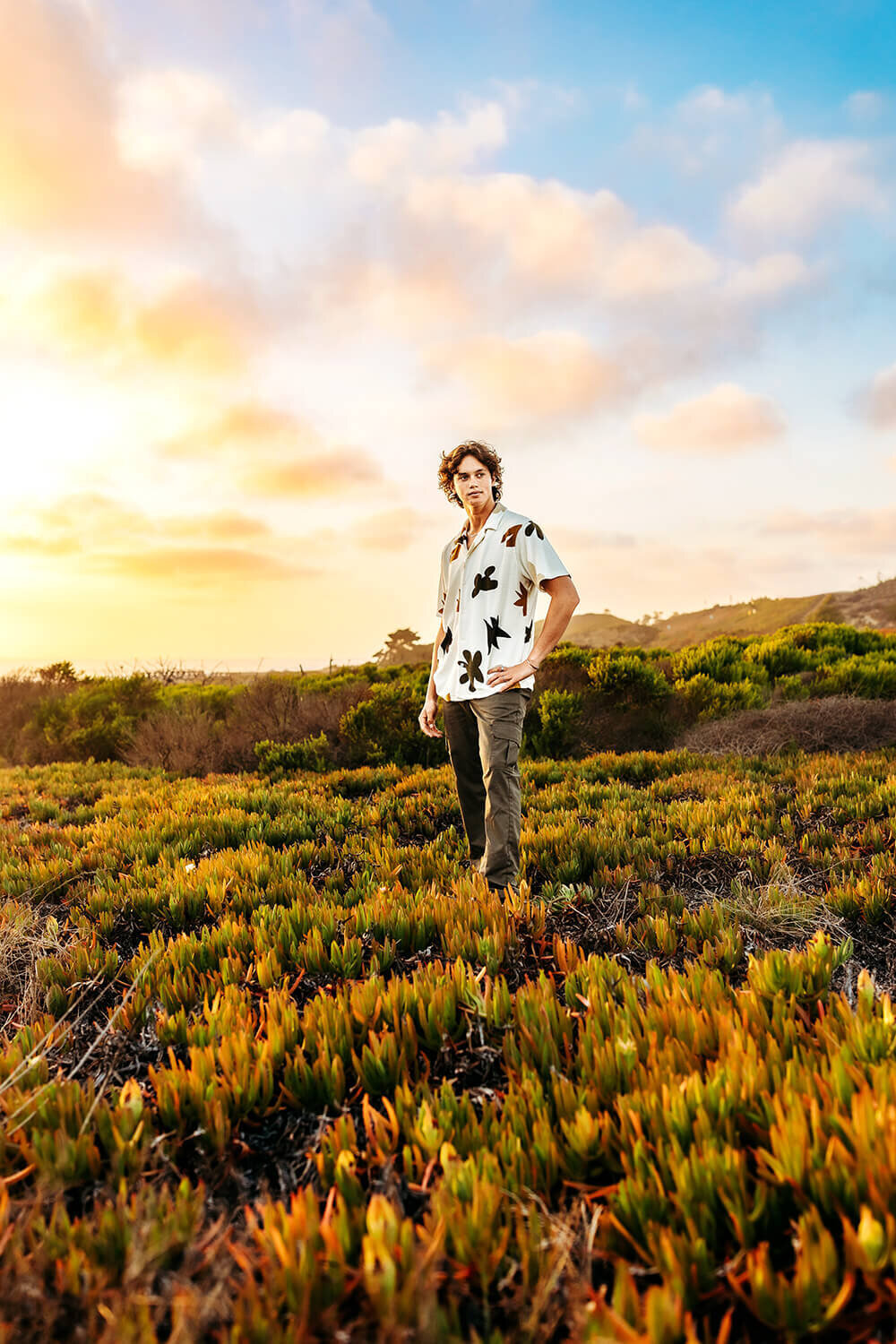 High school senior boy standing in the ice plants at sunset.