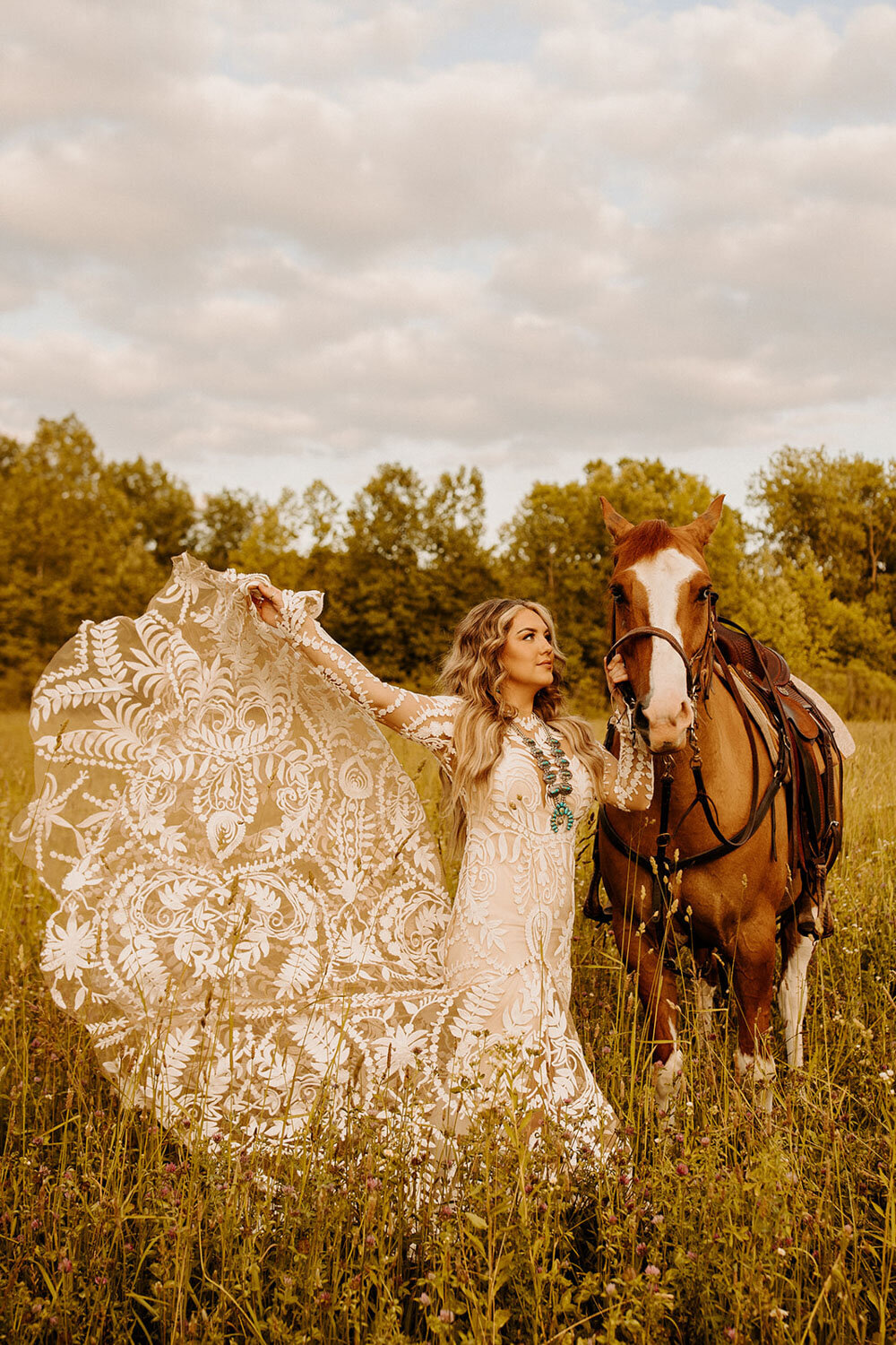 Bride holding horse's reins, wearing a lace gown in a field