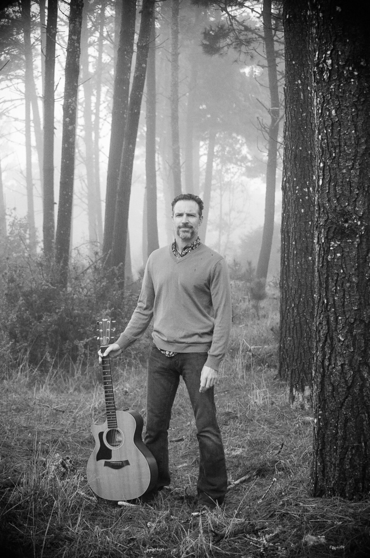 Musician holds his guitar in the foggy forest of Marin