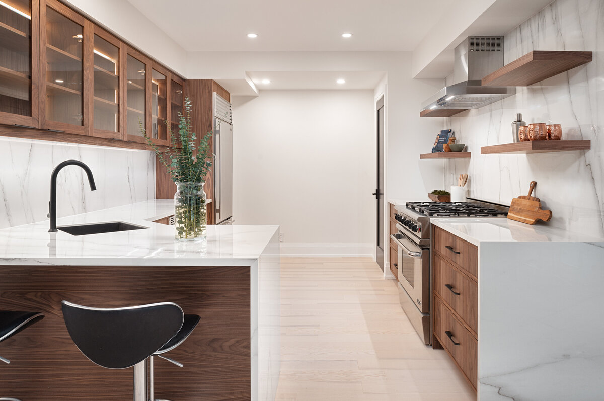 Kitchen condo design, the kitchen has dark wood cabinets with glass windows, waterfall marble countertops, with minimal decor.