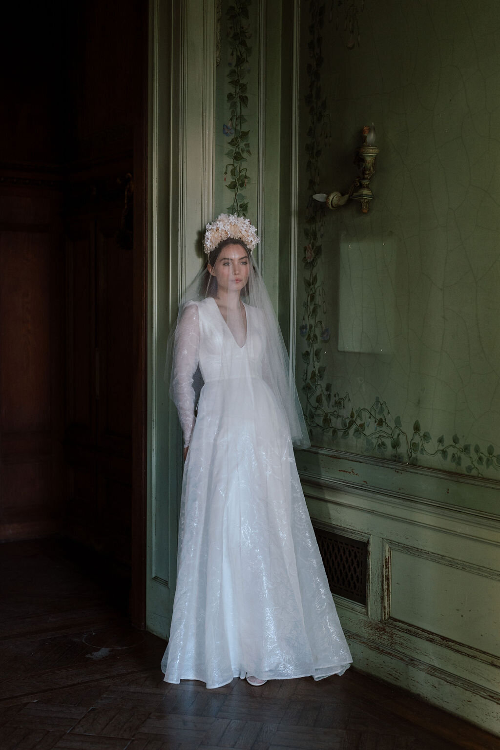 bride wearing wedding dress leaning against mansion wall