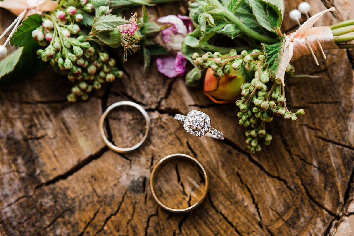 Pacific Northwest elopement photographer Amy Galbraith's image of a halo-style engagement ring and two wedding bands with flowers displayed on a wood stump