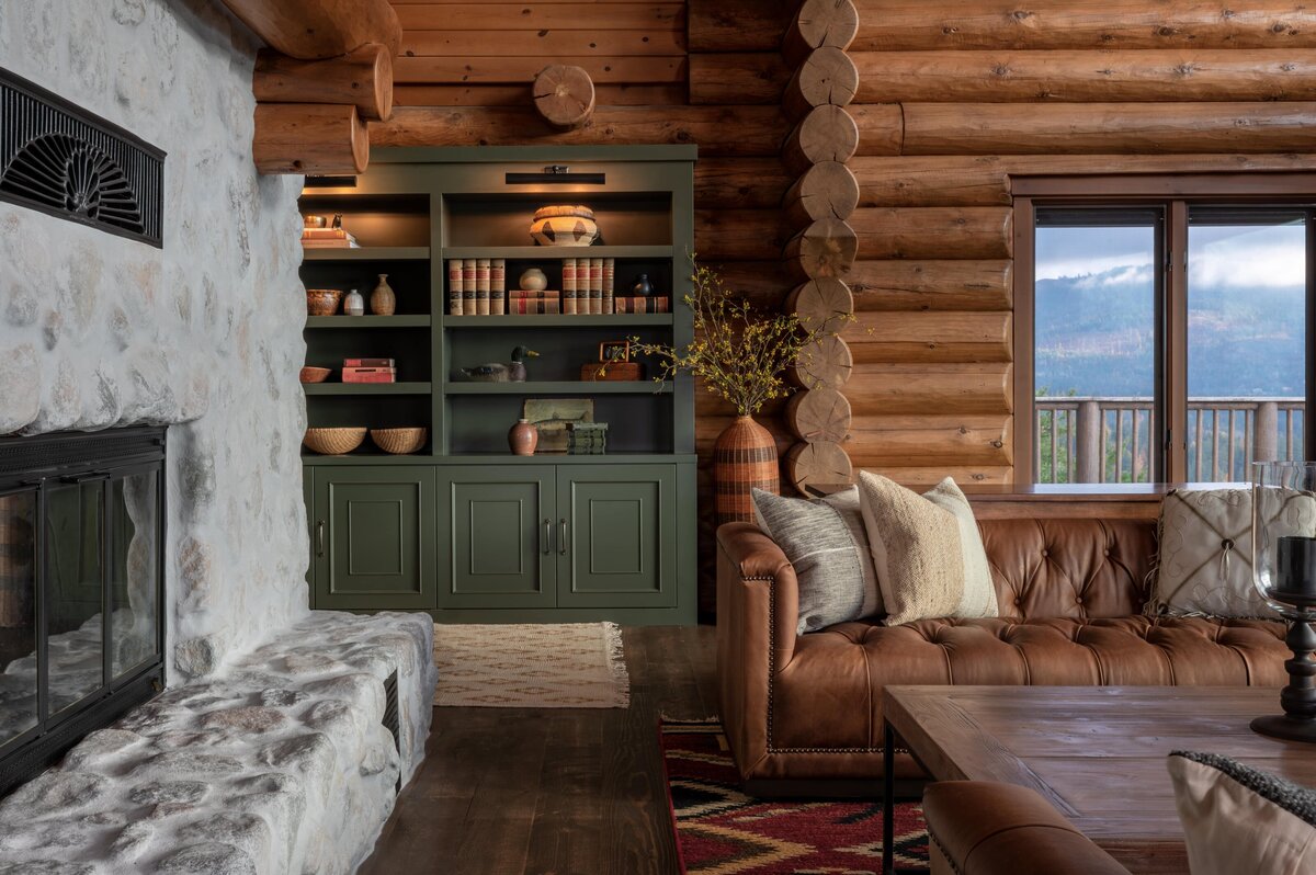 Rustic living room with stone fireplace, leather sofa, and custom built-ins, overlooking a mountain view in North Idaho.