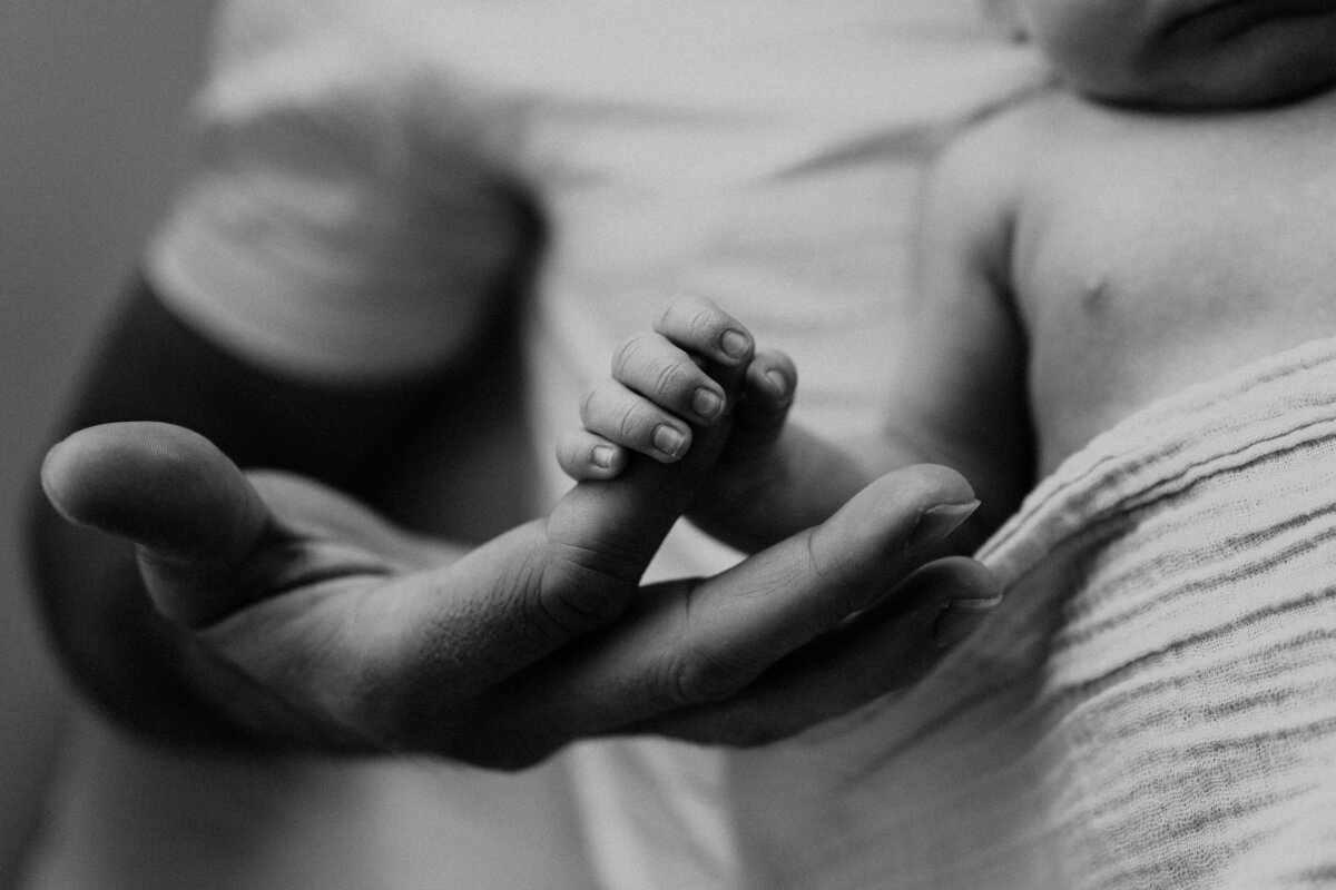 Dad holding newborn baby's hand in home newborn photography.