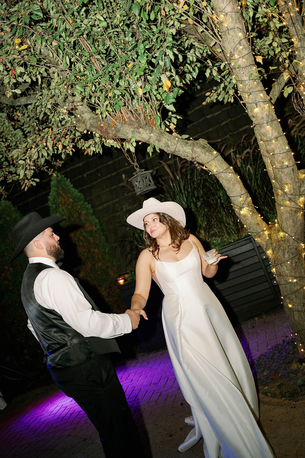 Bride and groom dancing under glowing garden lights at Café Cortina reception in Michigan, candid first dance moment.