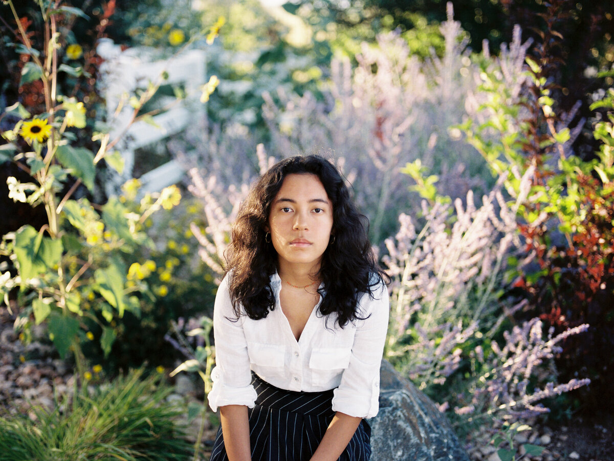 girl sits amongst purple flowers for high school portrait