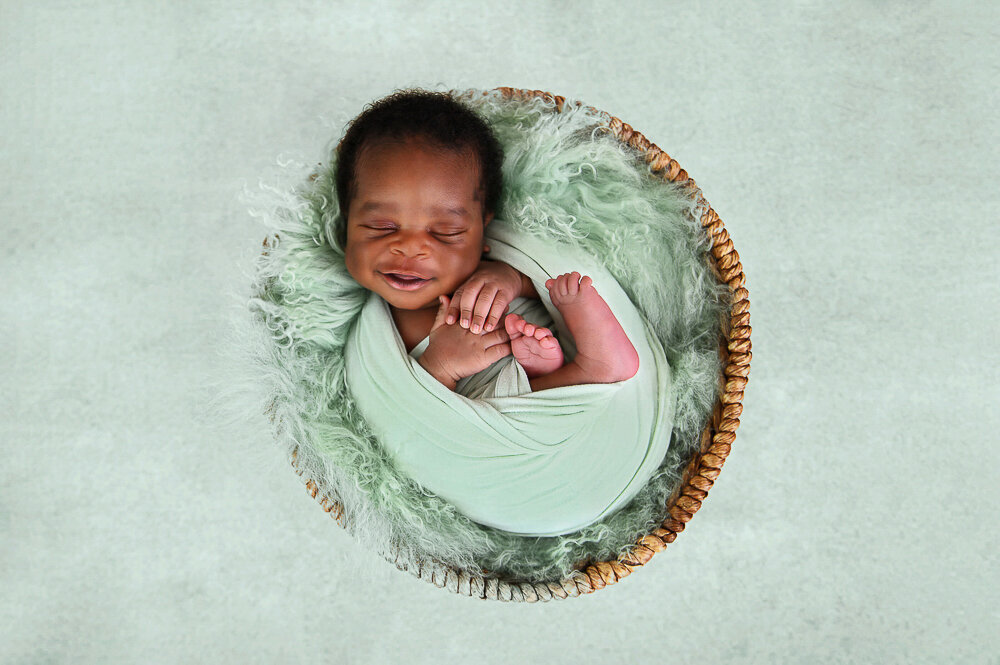 newborn boy wrapped in mint green smiling for his photos.