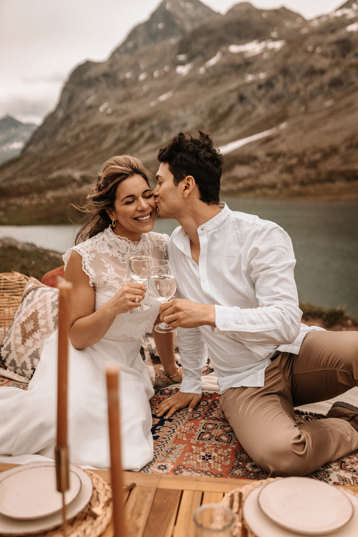 Brautpaar stößt an vor einem Gebirgssee in den Schweizer Alpen