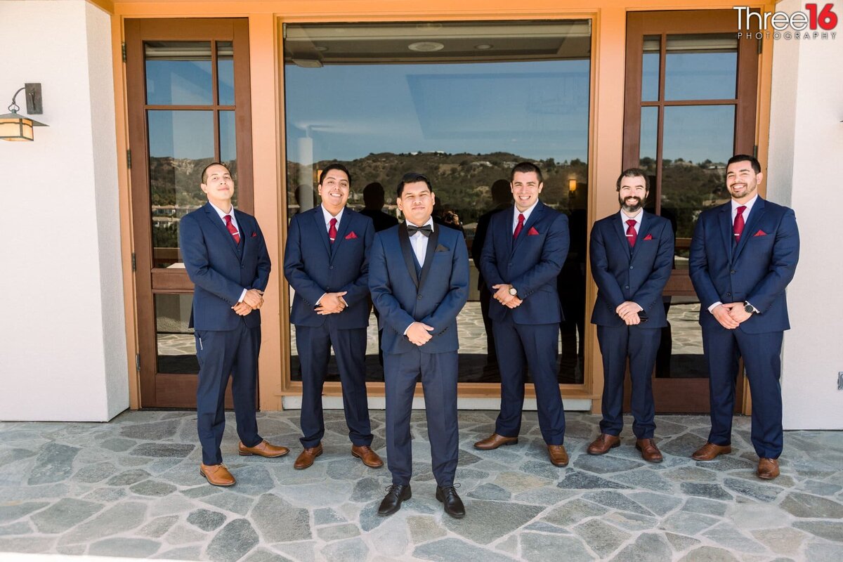Groom and his Groomsmen pose together holding their own hands in front of themselves with the Groom in the front